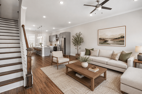 A living room with a staircase on the left side and a couch with a plant on it.