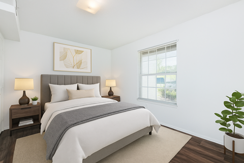 A bedroom with a large bed, two lamps, and a potted plant.