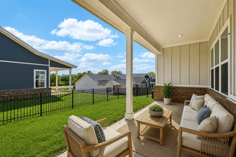 A patio with a sofa and chairs overlooking a green lawn and a blue house.