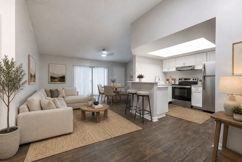 A modern living room with a white couch, a wooden coffee table, and a kitchen area in the background.
