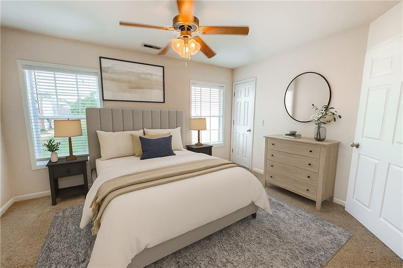 A bedroom with a large bed, a ceiling fan, and a nightstand with a lamp.