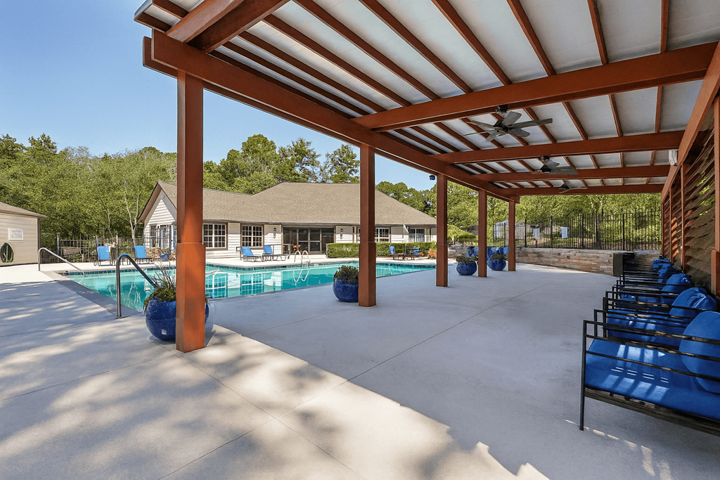 A pool area with a wooden pergola and blue lounge chairs.