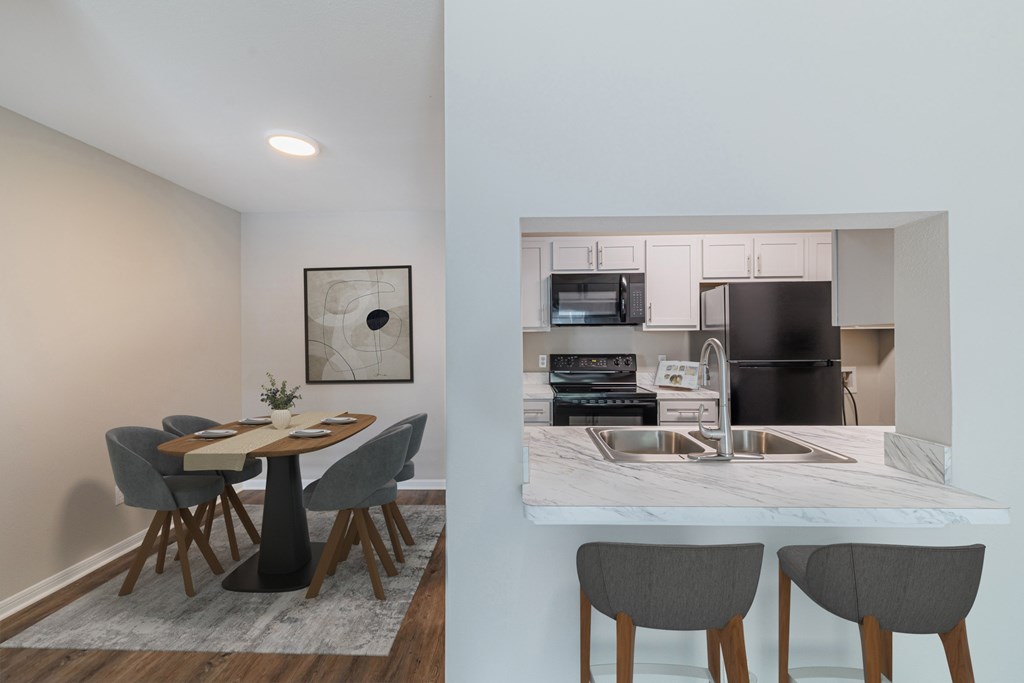 A kitchen with a table and chairs in the foreground and a microwave, oven, and sink in the background.