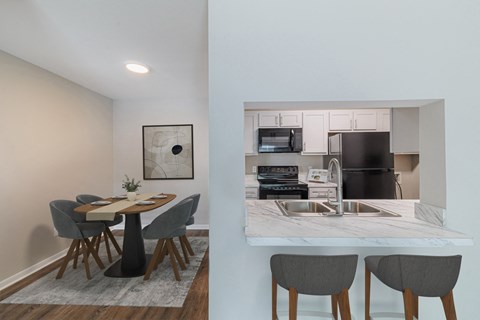 A kitchen with a table and chairs in the foreground and a microwave, oven, and sink in the background.