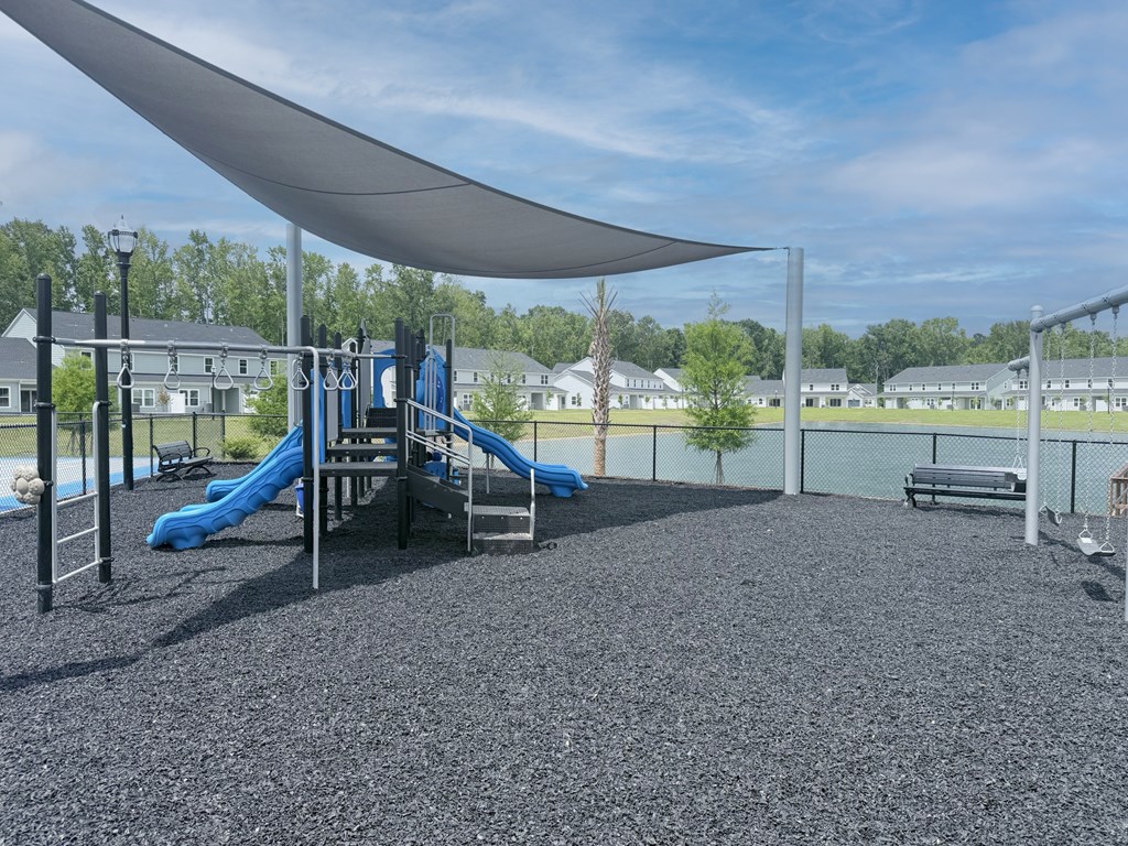 A playground with a blue slide and a white shade sail.