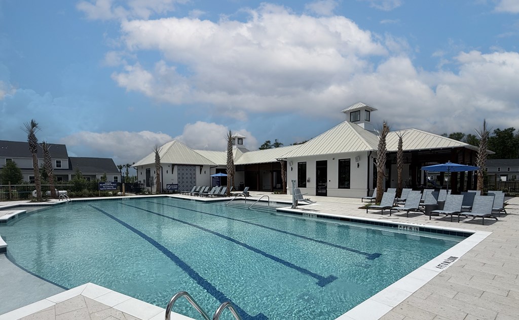 A large swimming pool with lounge chairs and a white building in the background.
