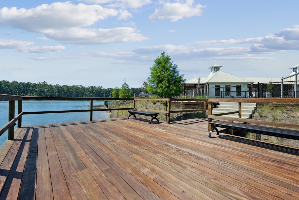 A wooden deck overlooks a body of water with a bench and a tree.
