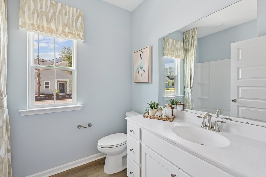 A bathroom with a white toilet, sink, and a window with a view of a house.