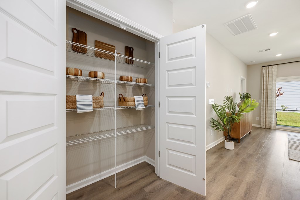 A white pantry with a glass door and shelves filled with baskets and plates.