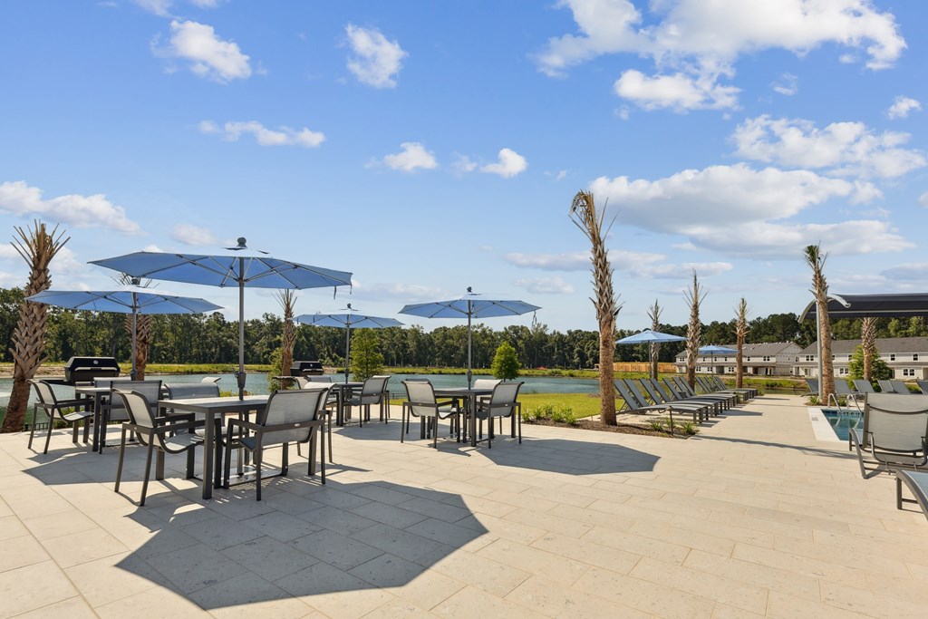 A patio with tables and chairs overlooking a lake.