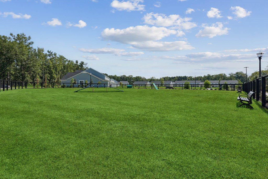 A large grassy field with a building in the distance and a bench on the right.