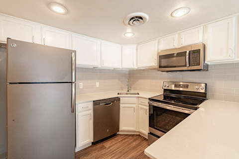 A kitchen with a refrigerator, microwave, oven, and sink.