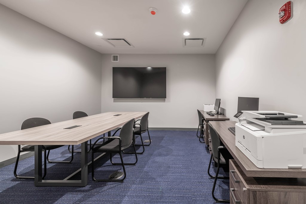 A conference room with a long table, chairs, and a projector screen.