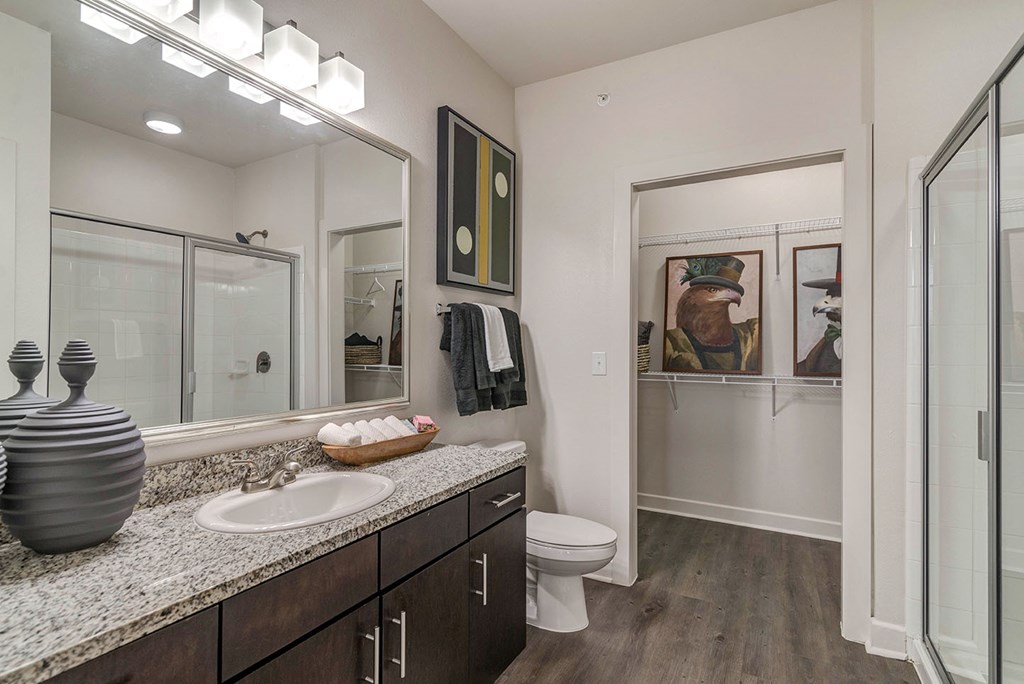 A bathroom with a sink, mirror, toilet and a wooden floor.