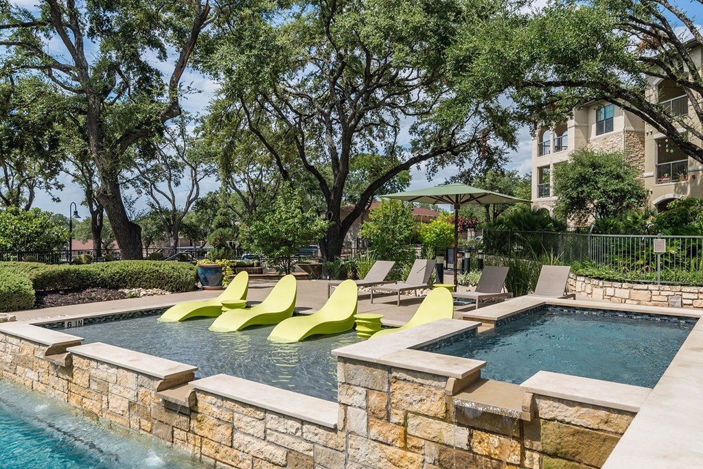 A pool with a stone wall and yellow chairs.