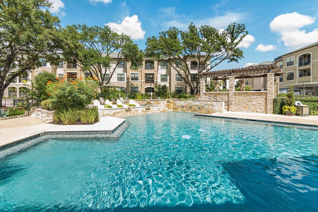 A swimming pool surrounded by a stone wall and trees.