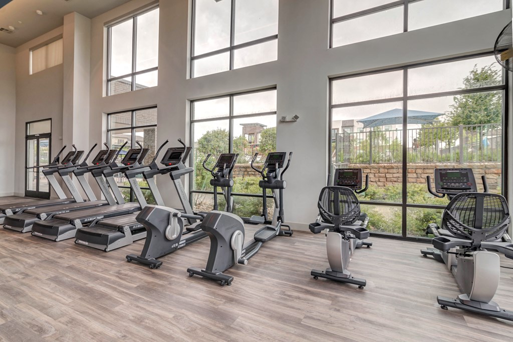 the fitness center has cardio machines and tall windows at the heights apartments