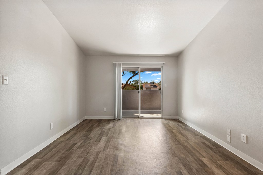 an empty living room with wood flooring and a door to a balcony