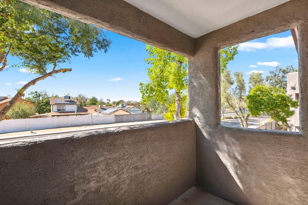 a large window on a balcony with a view of trees and houses