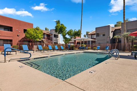 a swimming pool with blue lounge chairs and buildings in the background