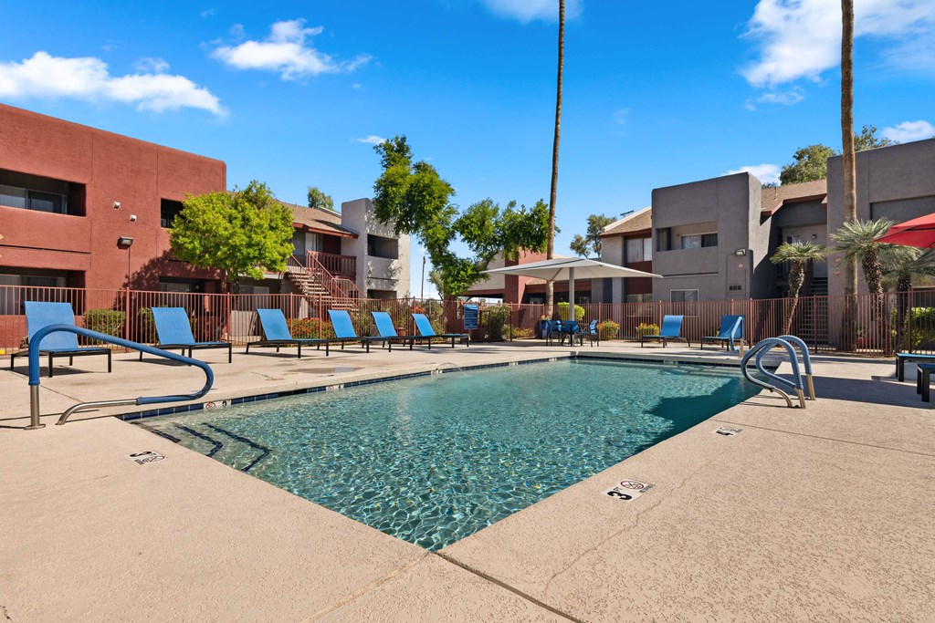 a swimming pool with blue lounge chairs and buildings in the background