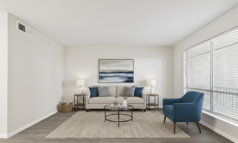 A living room with a white couch, a blue chair, and a painting on the wall.