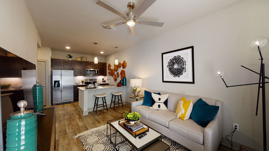 a living room with a couch and coffee table in front of a kitchen with a breakfast bar