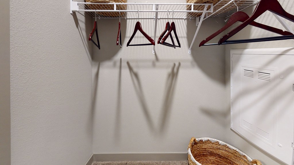 a walk in closet with a white closet organizer and a basket on the floor
