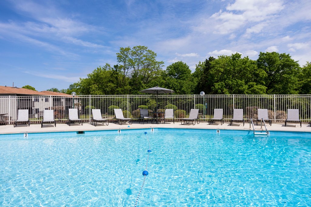 a swimming pool with chaise lounge chairs and umbrellas with trees in the background