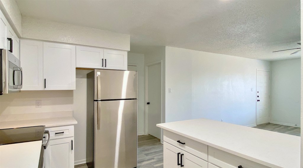 an empty kitchen with white cabinets and stainless steel refrigerator