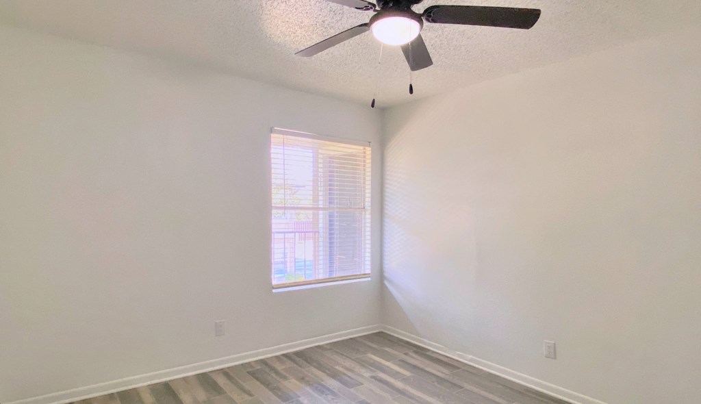 an empty bedroom with a ceiling fan and a window