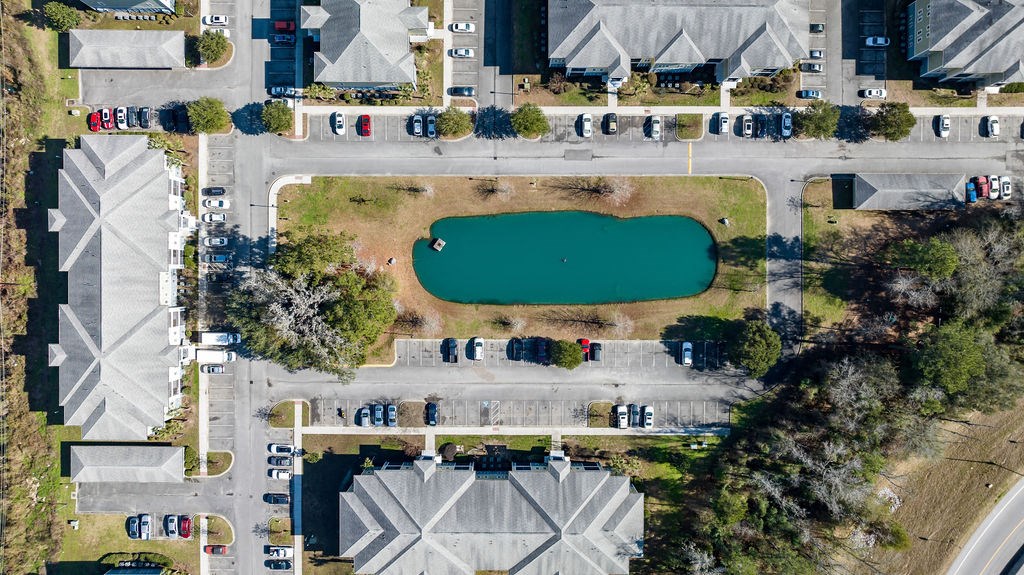 A bird's eye view of a parking lot with cars and a pond.