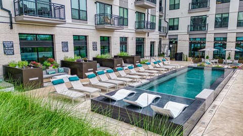 an outdoor pool with lounge chairs and umbrellas in front of an apartment building