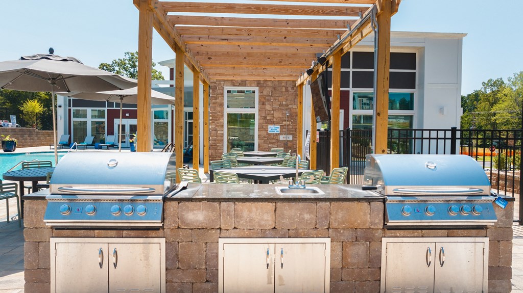 two bbq grills with umbrellas and a pool in the background