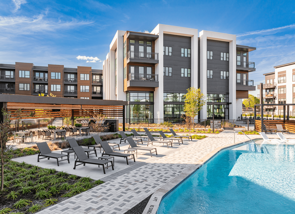 A modern apartment complex with a pool and lounge chairs.