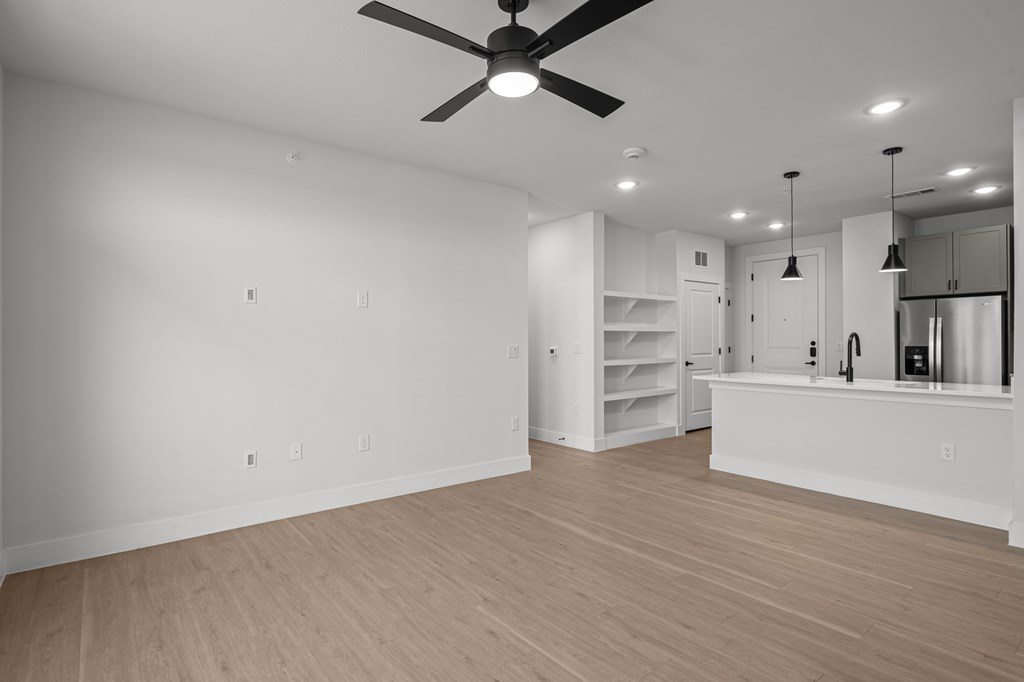 A spacious, empty room with a ceiling fan and lighting fixtures.