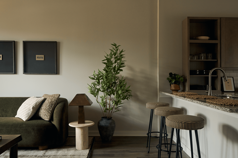 A living room with a green couch, a table with a lamp, and a bar area with stools.