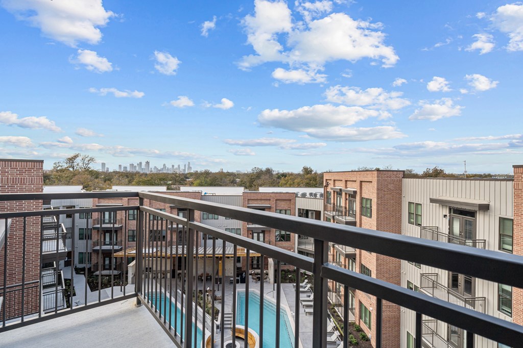 A balcony with a pool and buildings in the distance.