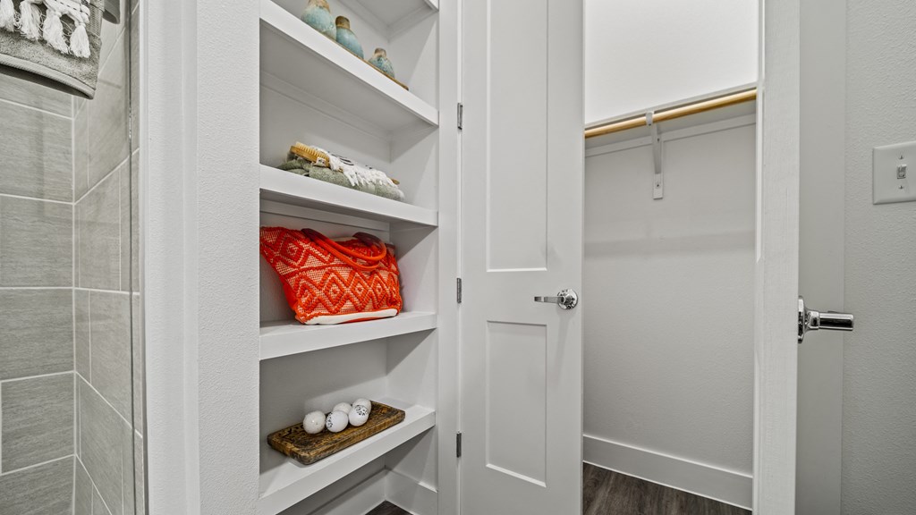 a walk in closet with white cabinets and shelves and a white door