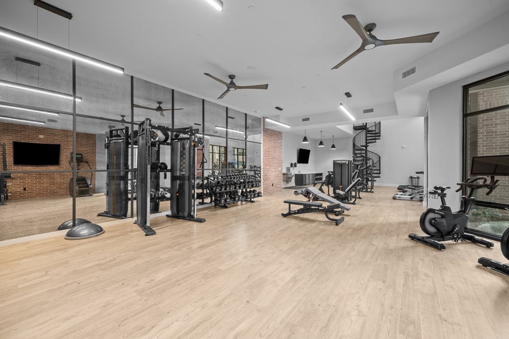 A gym with a variety of equipment including treadmills, weights, and a spiral staircase.