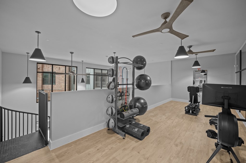 A room with a wooden floor and a white ceiling with a fan, and a rack of exercise equipment.