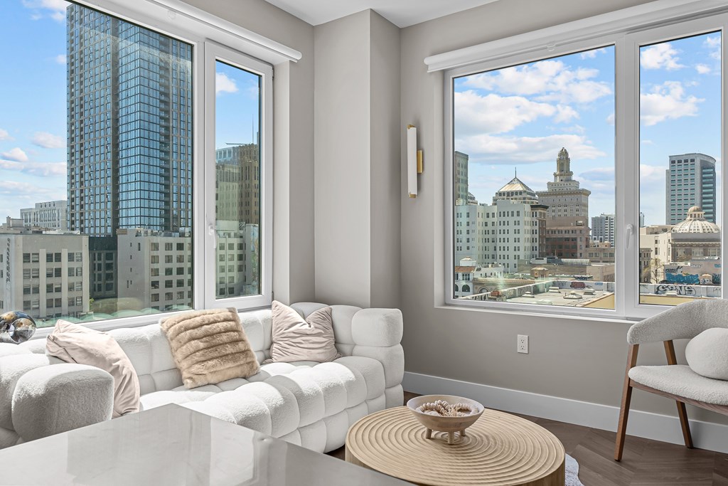 A white couch with a pillow and a bowl on a table in front of a window.