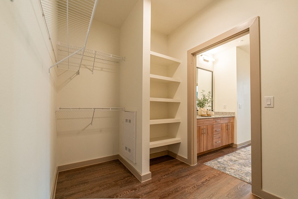 A room with a white wall and a wooden floor with a white shelf and a mirror.