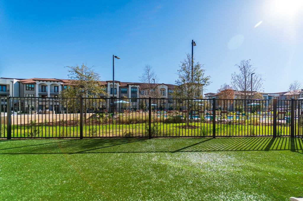A sunny day at a park with a black fence and a building in the background.
