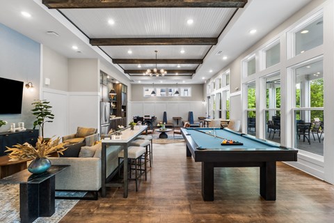 A pool table is in the middle of a room with a bar and a TV.