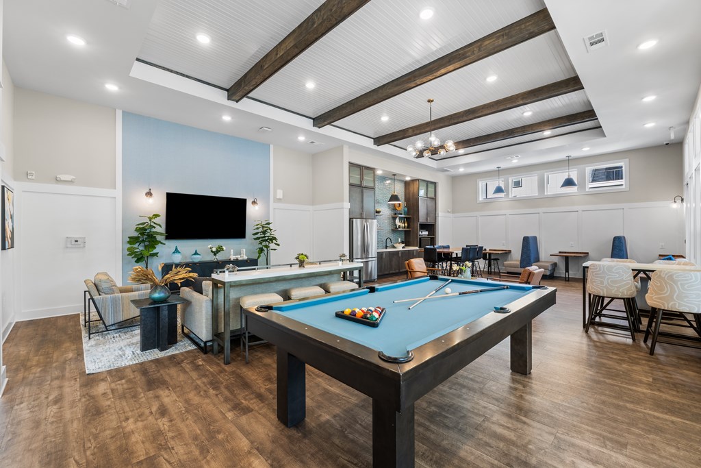 A pool table is in the middle of a room with a TV and a bar.