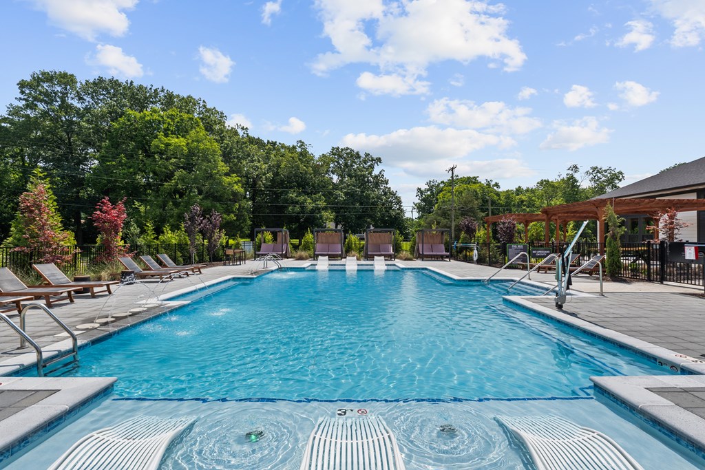 A large swimming pool with a hot tub in the middle surrounded by trees.