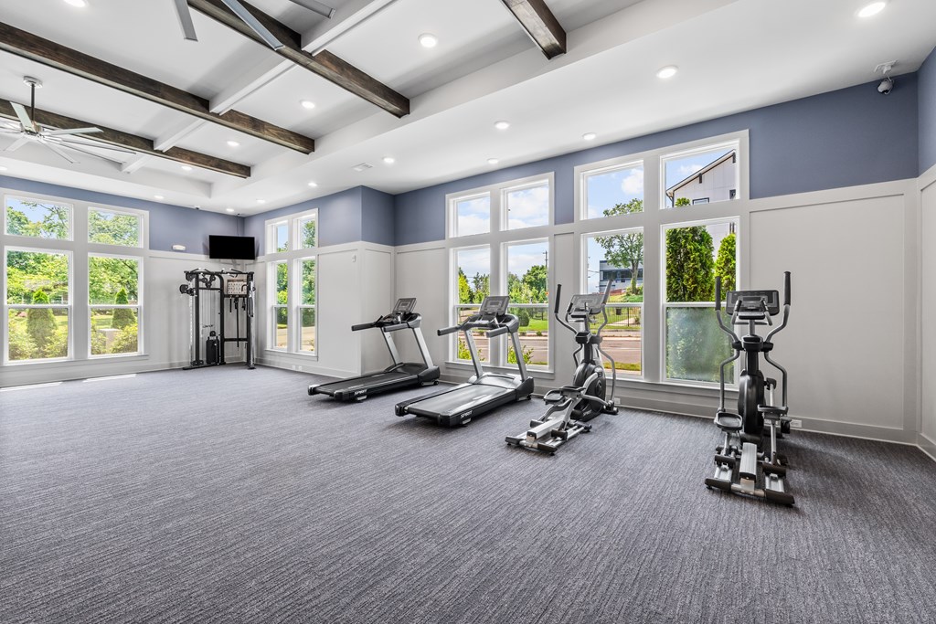 A spacious gym with treadmills, elliptical machines, and a television.