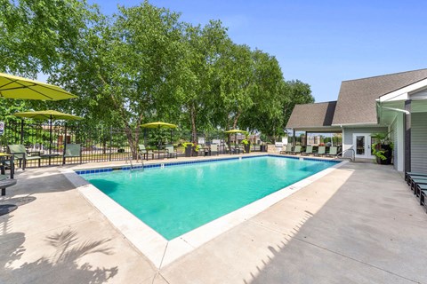 A large outdoor swimming pool surrounded by trees and umbrellas.
