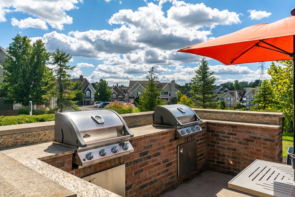 Two grills on a patio with a red umbrella above.